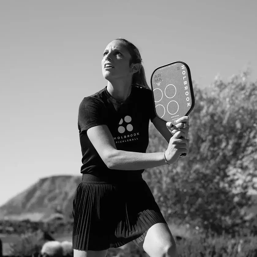 Woman playing pickleball with Holbrook paddle, showcasing the ARMA design in a scenic outdoor setting.