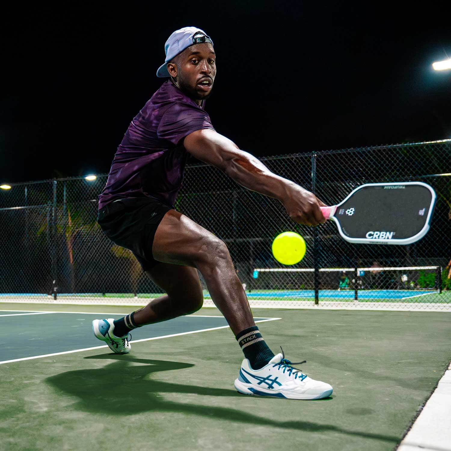 Player showcasing CRBN TruFoam Genesis paddle while hitting a ball on a well-lit pickleball court.