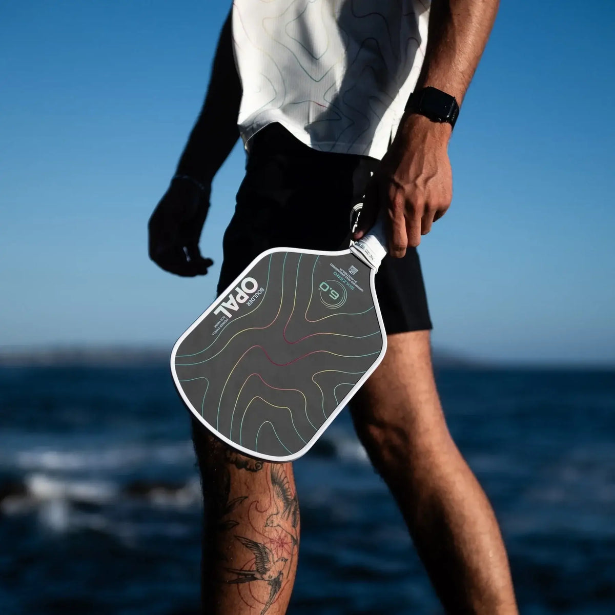 Six Zero Boulder Opal 14mm paddle held by a player near the water showcasing its sleek design and advanced technology.