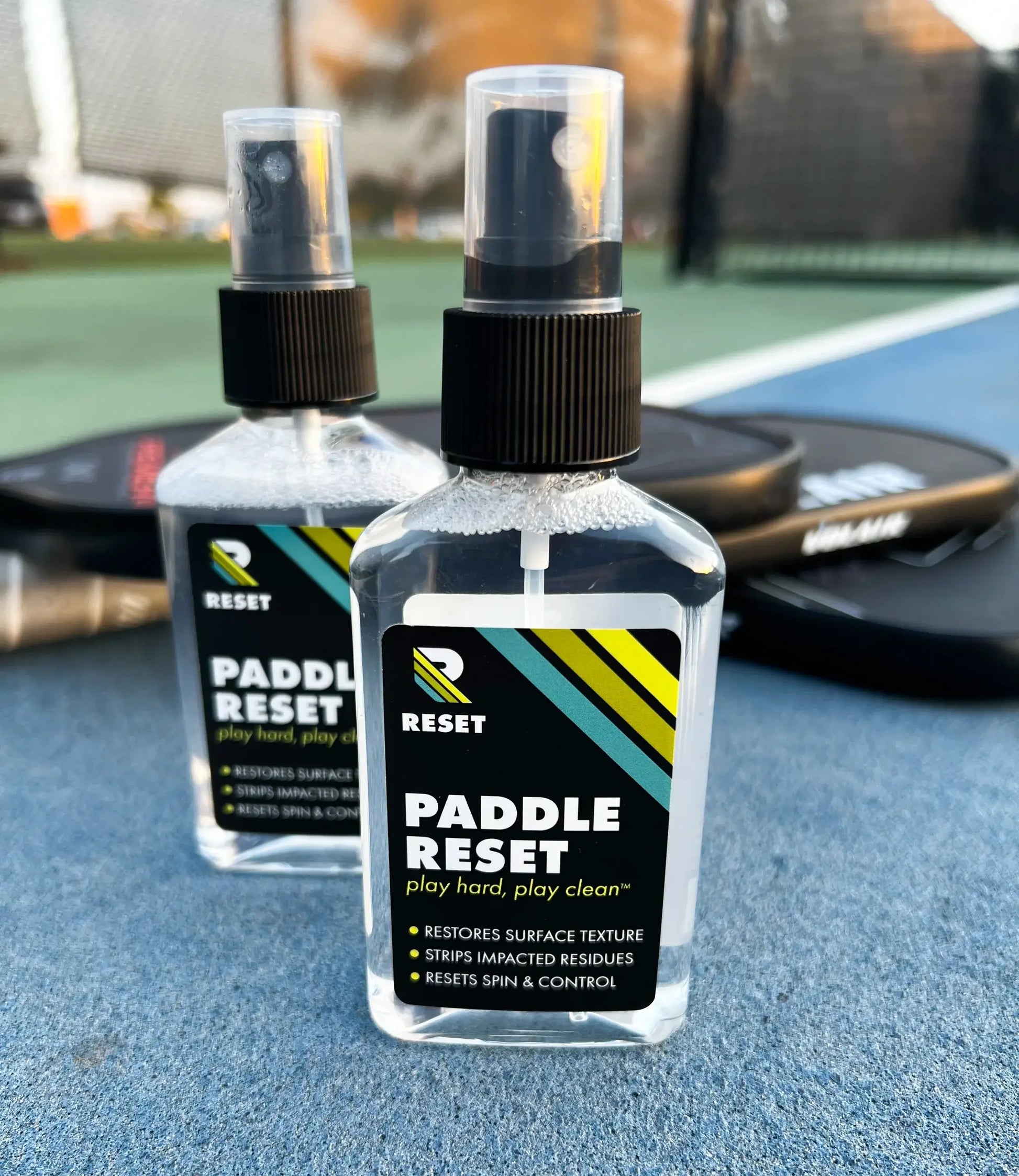 Paddle Reset spray bottles on a tennis court, designed to restore surface texture and enhance paddle performance.