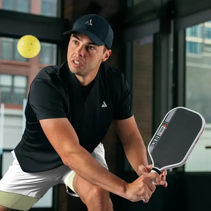 Male player hitting a pickleball with JOOLA Ben Johns Perseus Pro IV paddle in a dynamic indoor setting.