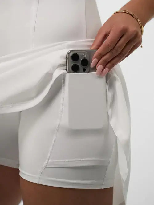 Close-up of a hand placing a smartphone into the pocket of a white athletic dress, showcasing functional design.