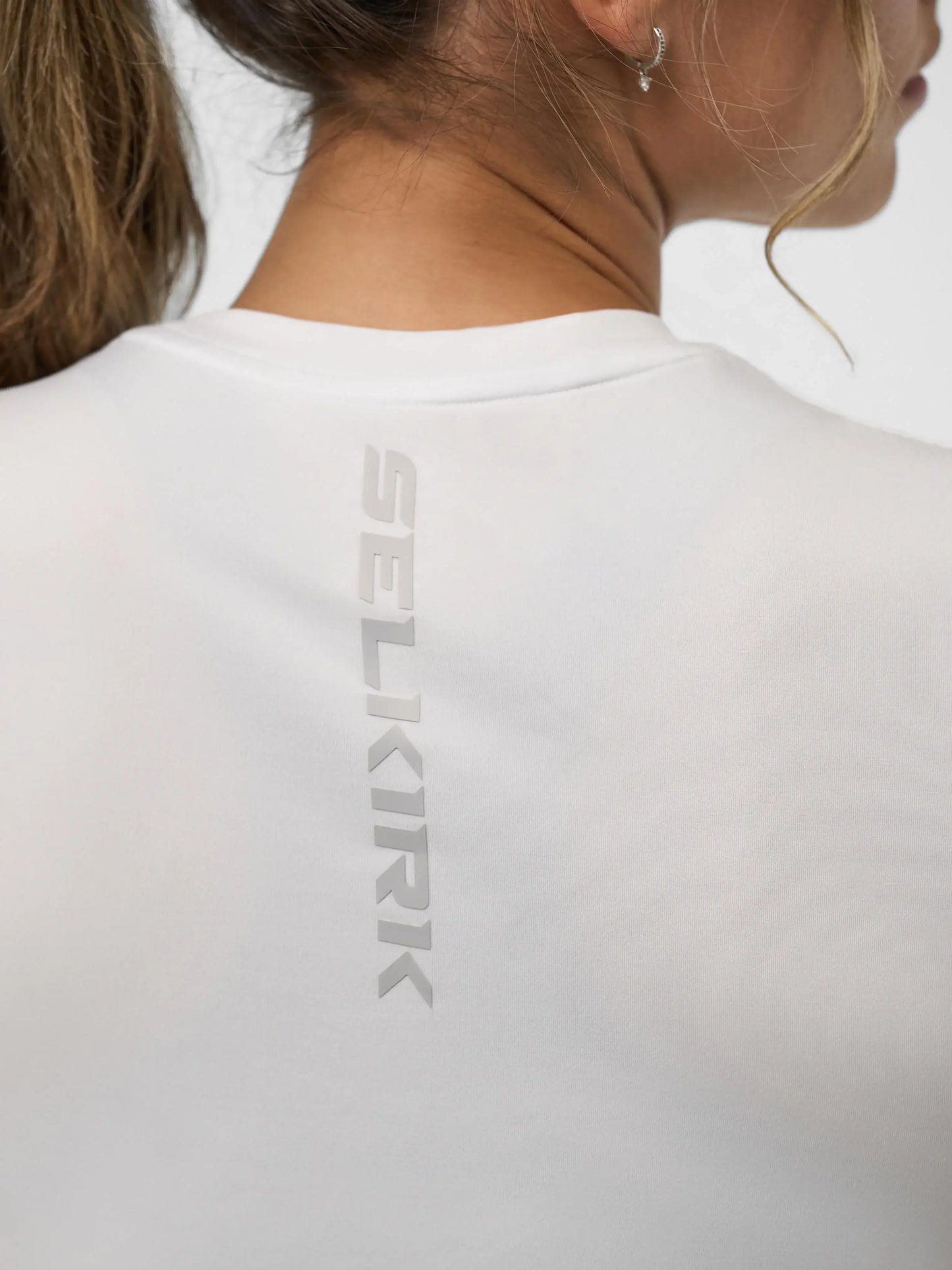Close-up of Selkirk Sport logo on the back of a women's white training tee, showcasing its stylish design.