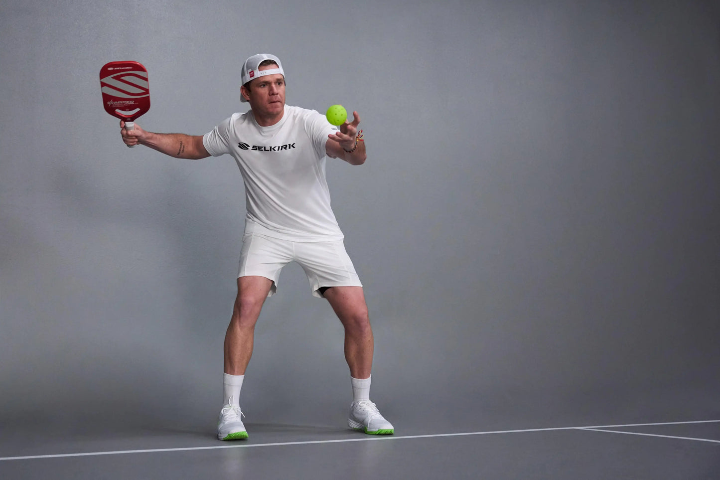 Player preparing to hit a pickleball with the Selkirk AMPED Pro Air paddle on a court background.
