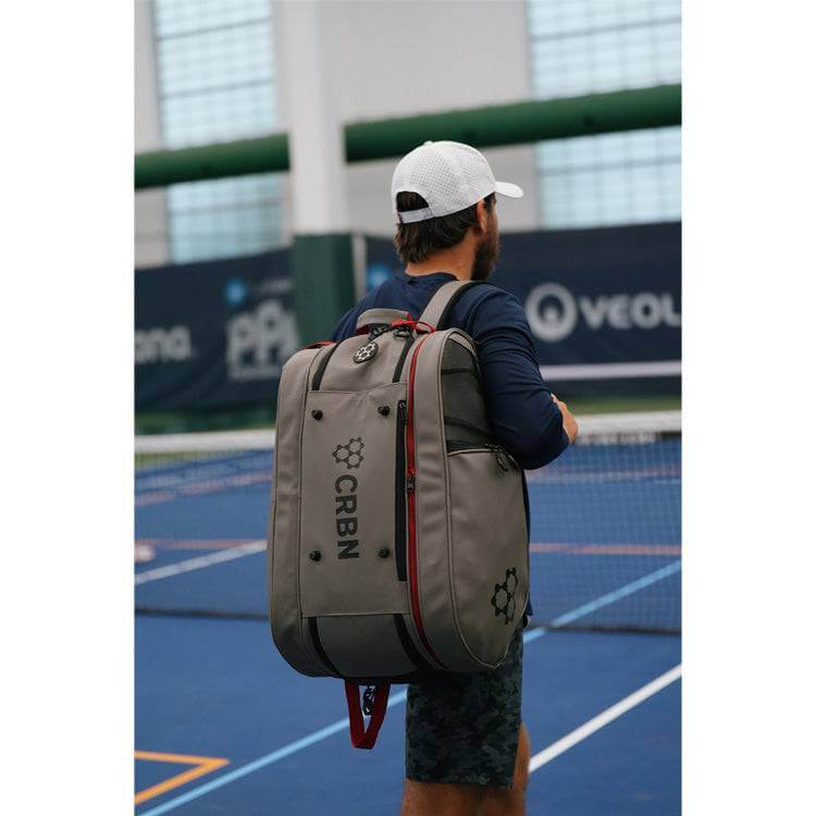 Person carrying the CRBN Pro Team Tour Bag 2.0 on the tennis court, showcasing its spacious design and functionality.