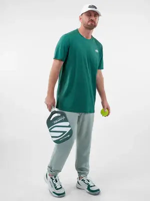 Man wearing a green short sleeve performance tee, holding a pickleball paddle and ball, ready for a game.