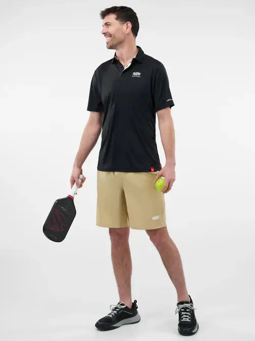 Man in black Sport-Wik polo ready for pickleball, holding a paddle and ball, wearing beige shorts and athletic shoes.