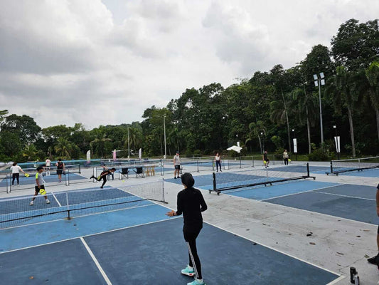 Outdoor pickleball courts at University Malaya with players engaged in games, surrounded by greenery and clear sky.