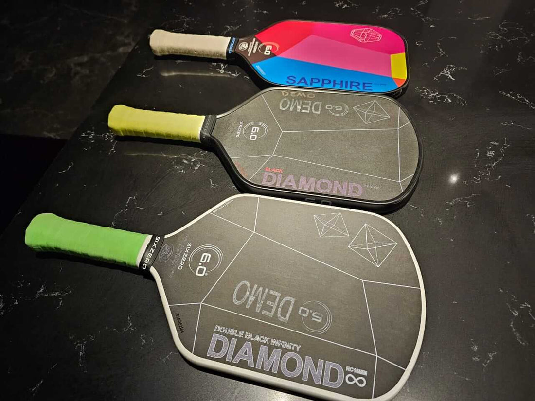 Three premium pickleball paddles on a dark surface, including models Sapphire and Diamond from Six Zero. 