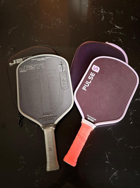 Two pickleball paddles with protective covers on a black surface, showcasing modern designs and new face materials.