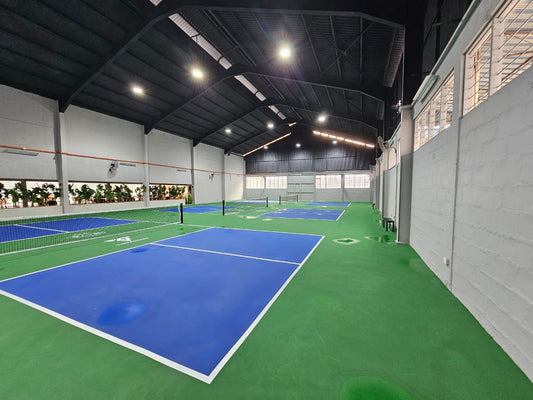 Indoor pickleball courts at Pickleball Factory, Subang SS13, featuring blue playing surfaces and surrounding greenery.