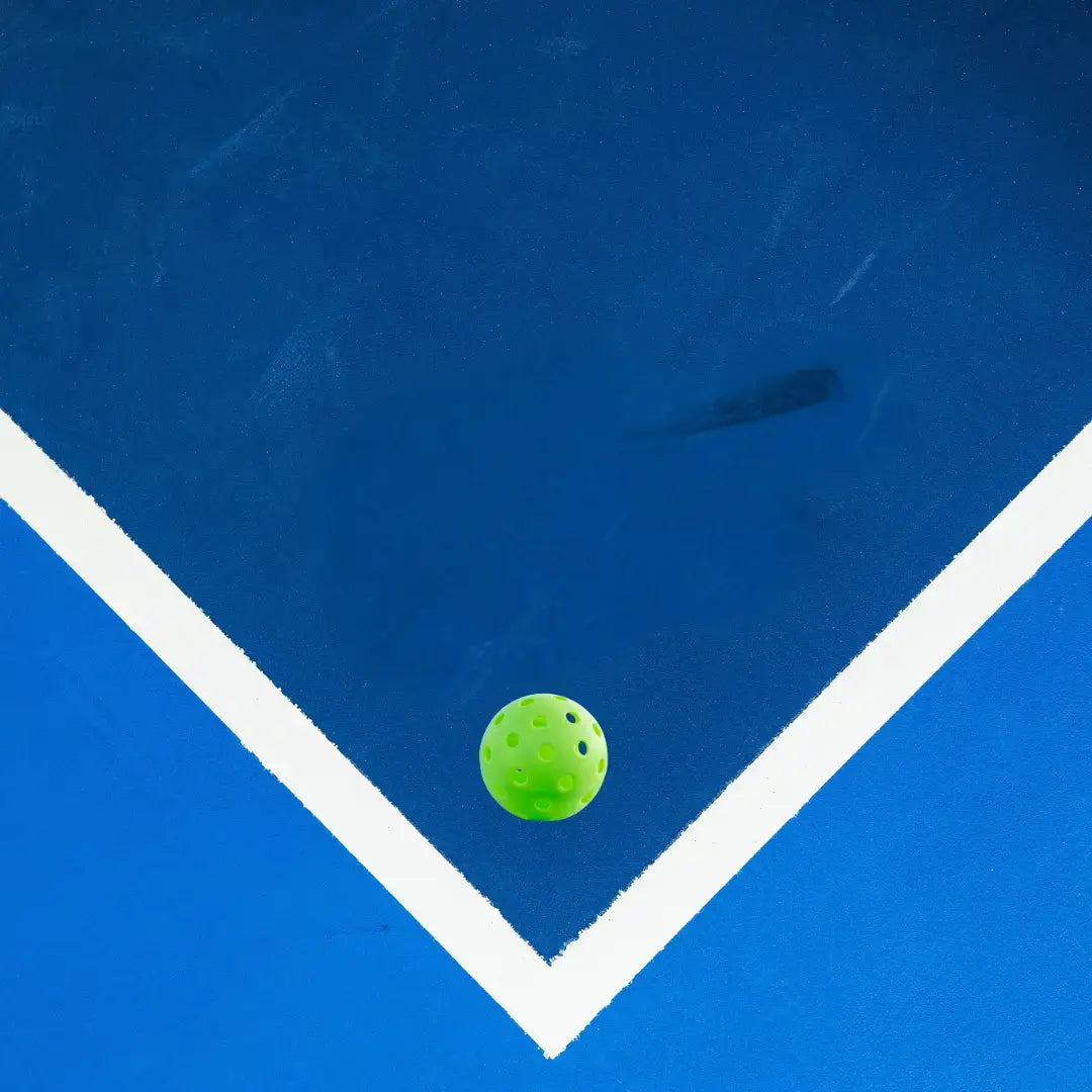 Close-up of a bright green pickleball resting in the corner of a blue pickleball court.