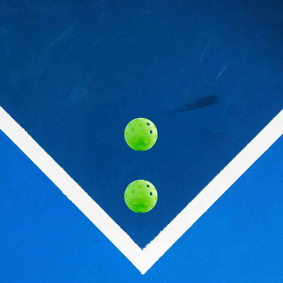 Two green pickleballs on a blue court surface, emphasizing the importance of quality equipment for improved player performance.