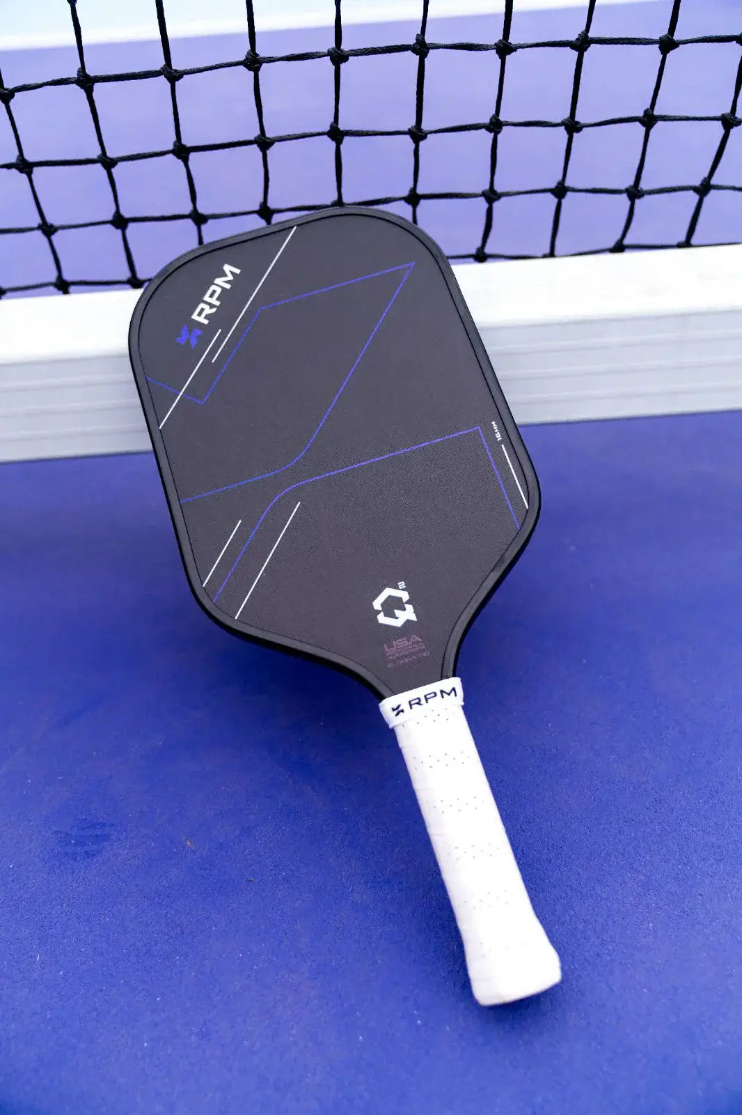 RPM Q2 Elongated Paddle - 16MM on a blue surface with a net in the background.