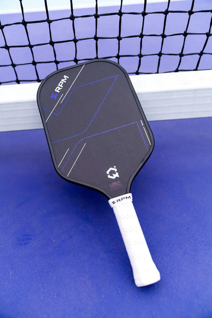 RPM Q2 Elongated Paddle - 16MM on a blue surface with a net in the background.