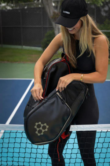 Woman holding CRBN Pro Team Tour Bag 2.0 on a court, showcasing its sleek design and functionality.