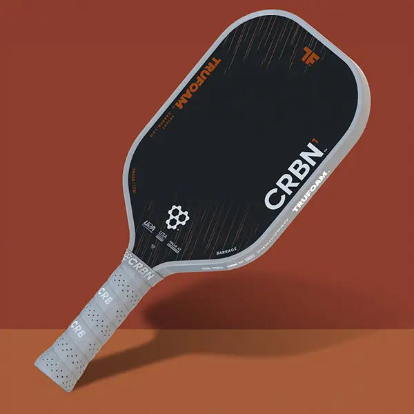 CRBN¹ TruFoam Barrage (Elongated, Long Handle) paddle with black surface and grey handle on a warm background.
