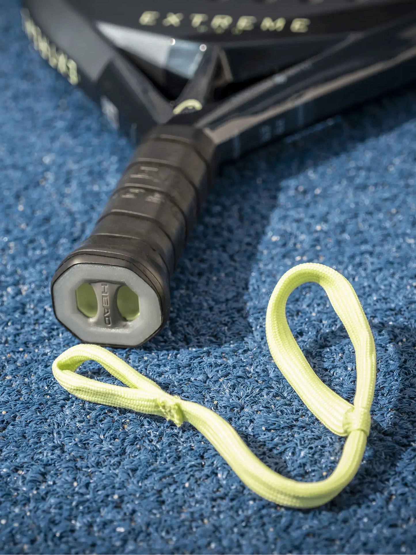 HEAD Extreme Pro Padel Racquet handle with safety strap on blue court surface.