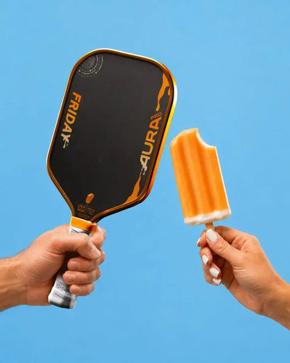Friday Aura Pro -  Elongated (Limited Metallic Series) paddle held alongside a popsicle against a blue background.