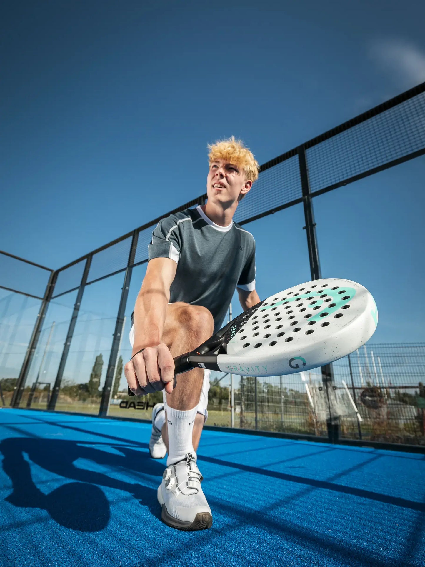 Player demonstrating skill on a padel court with HEAD Gravity Pro Padel Racquet under clear blue sky.