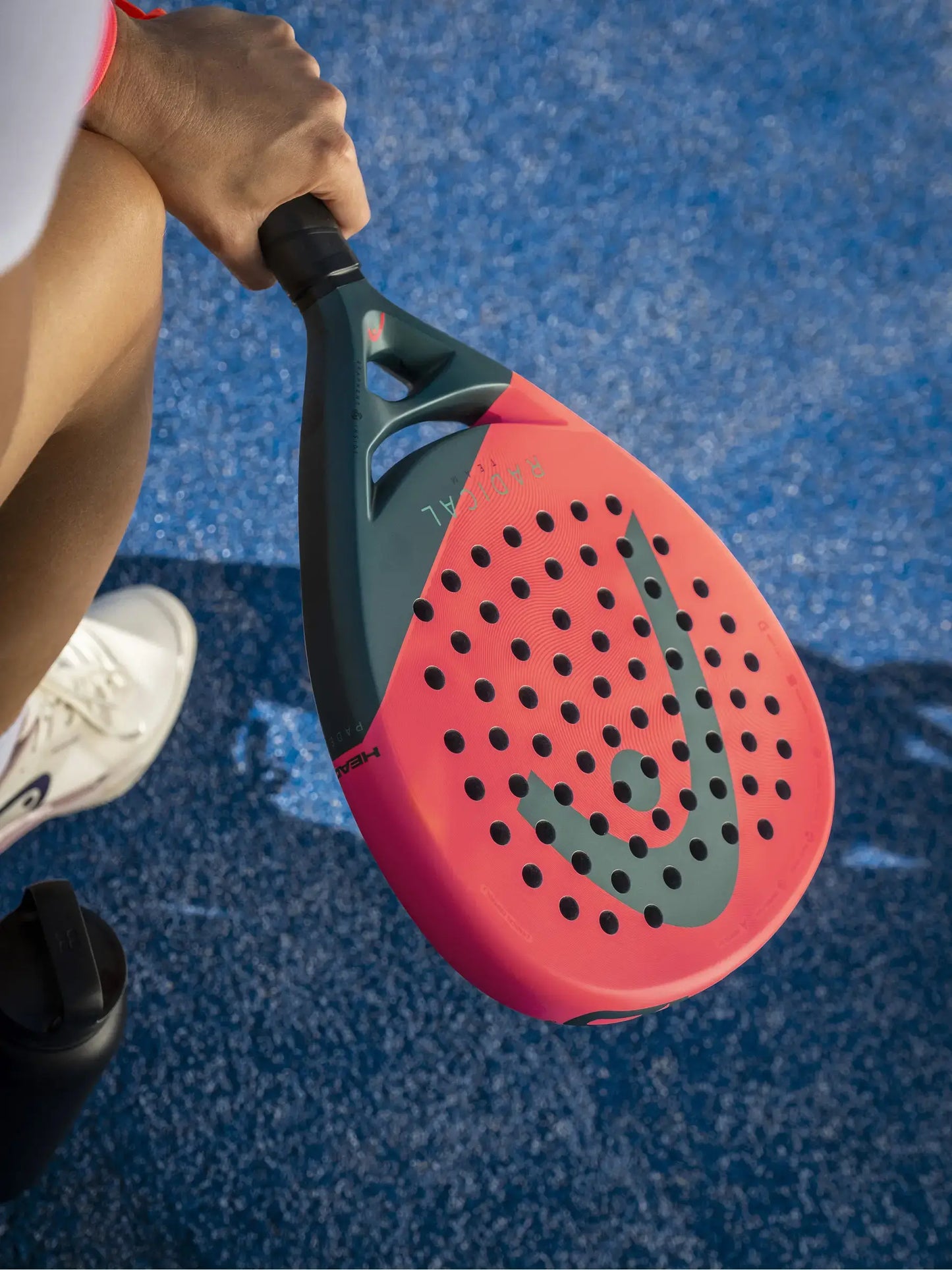 HEAD Radical Team Padel Racquet held by a player on a blue court, showcasing the striking design and perforations.