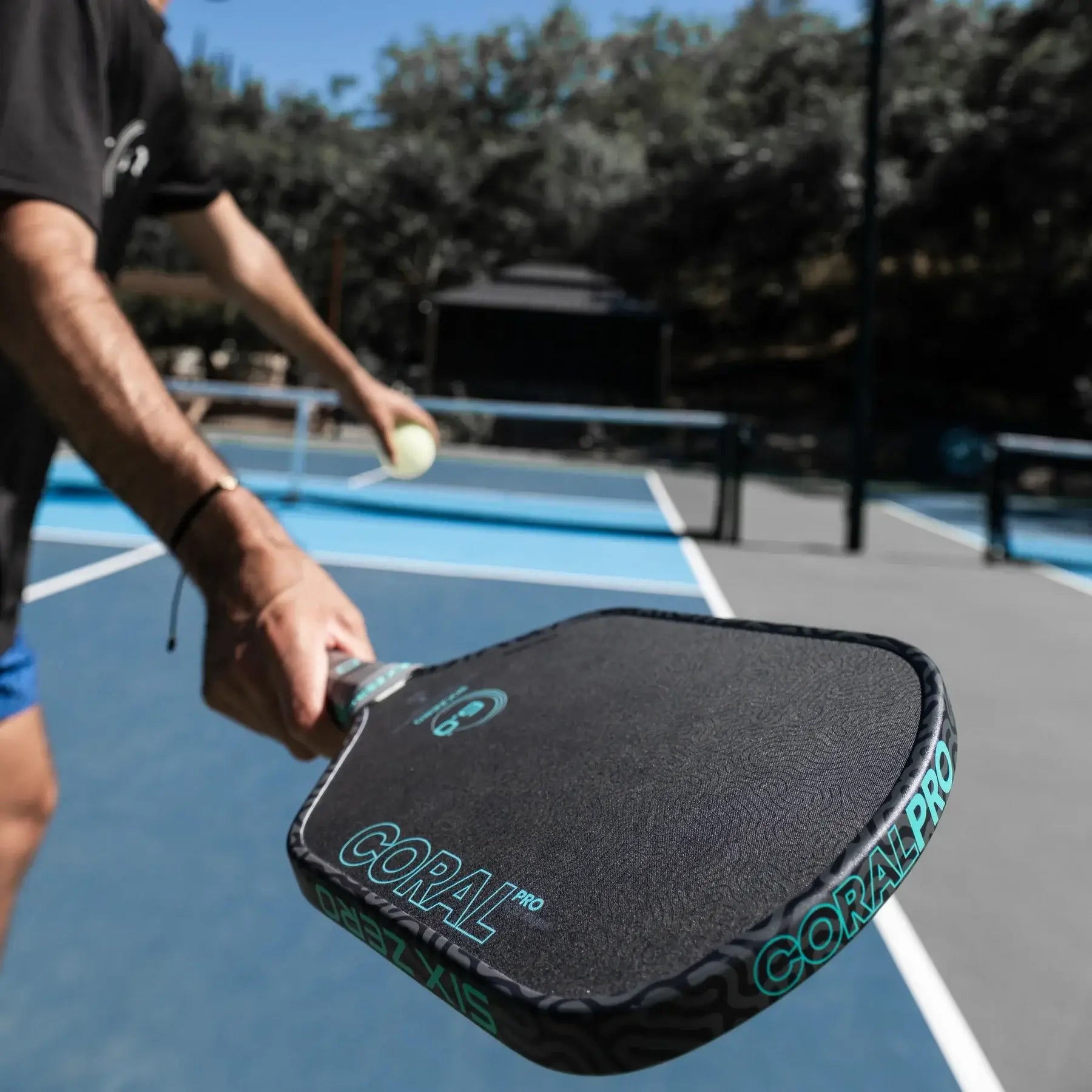 Player serving with the Six Zero Coral Pro 16mm paddle on a tennis court, showcasing its advanced design and grip.